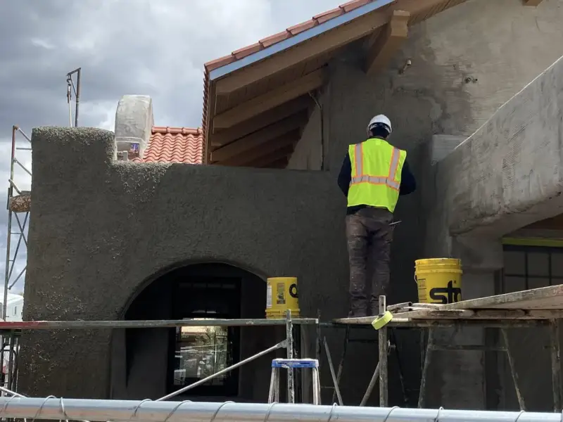 Plasterer on scaffolding applying stucco to a stepped parapet wall