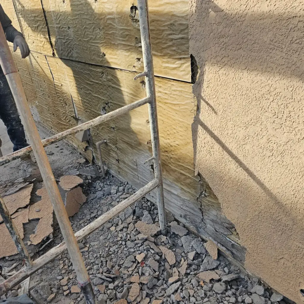 Close-up of torn-off stucco pieces on the ground and foam substrate on the wall