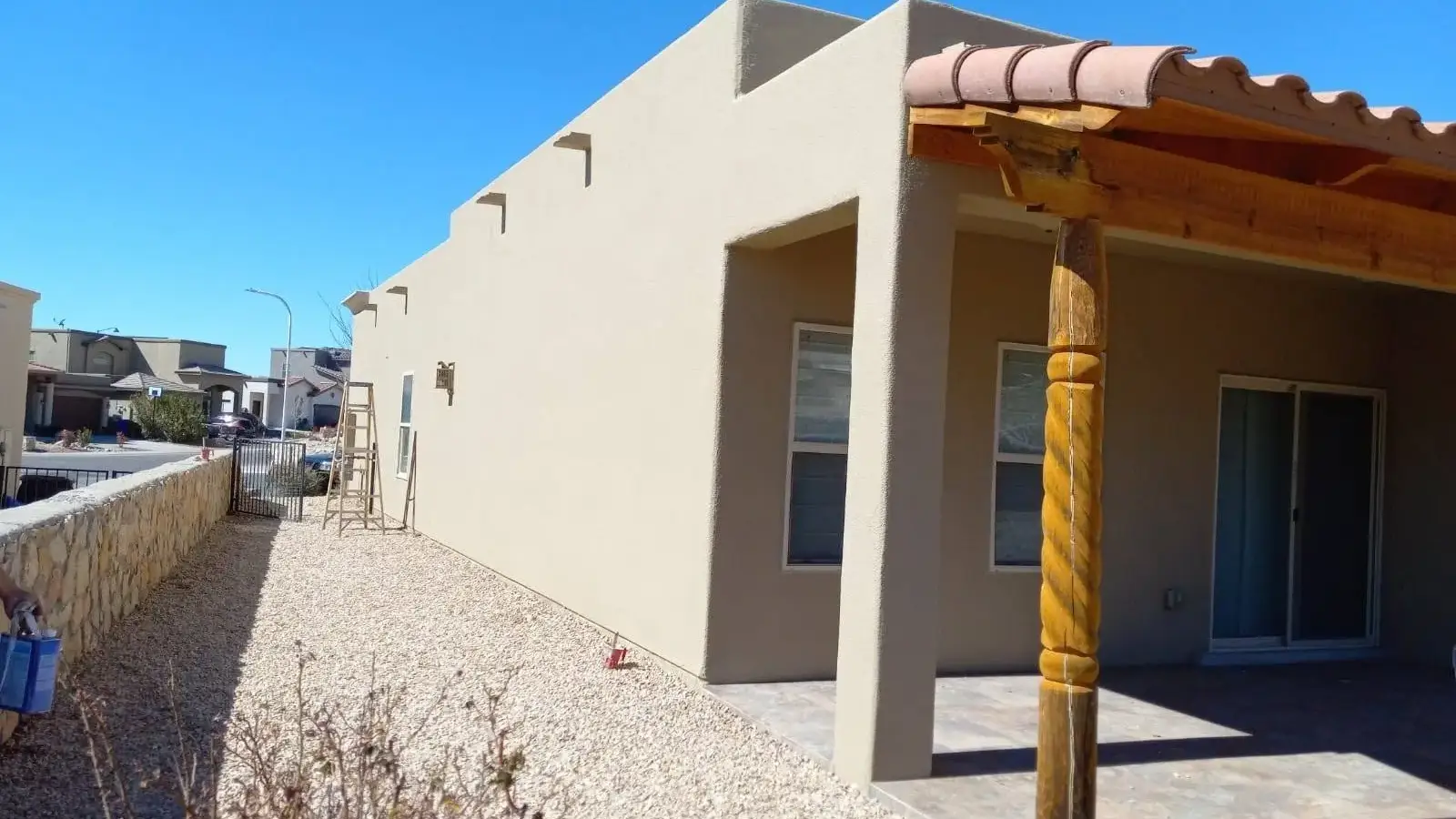 Long stucco wall with a smooth tan finish and a wood portal with carved posts