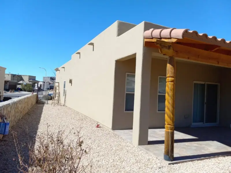 Long stucco wall with a smooth tan finish and a wood portal with carved posts