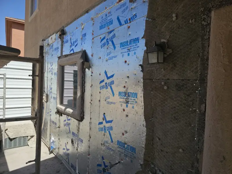Wall opened around a window showing foam insulation board, weather barrier and wire lath