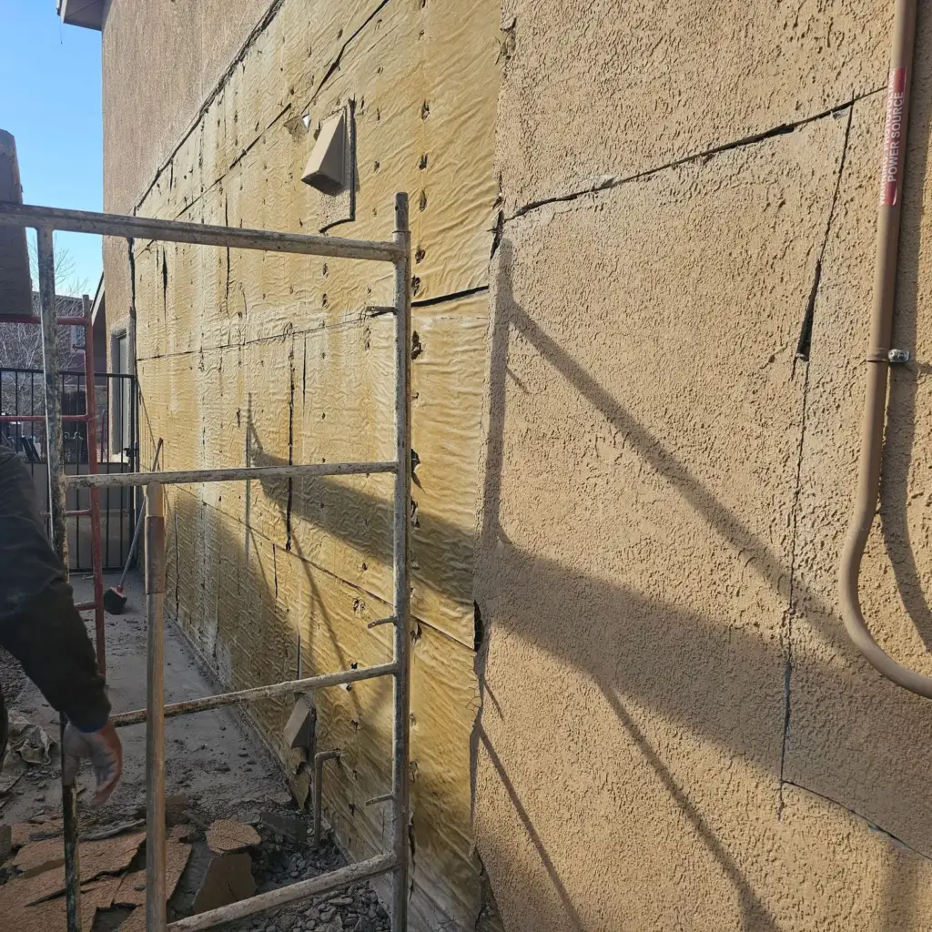 Stucco wall with the finish torn away showing foam board joints and a crack line