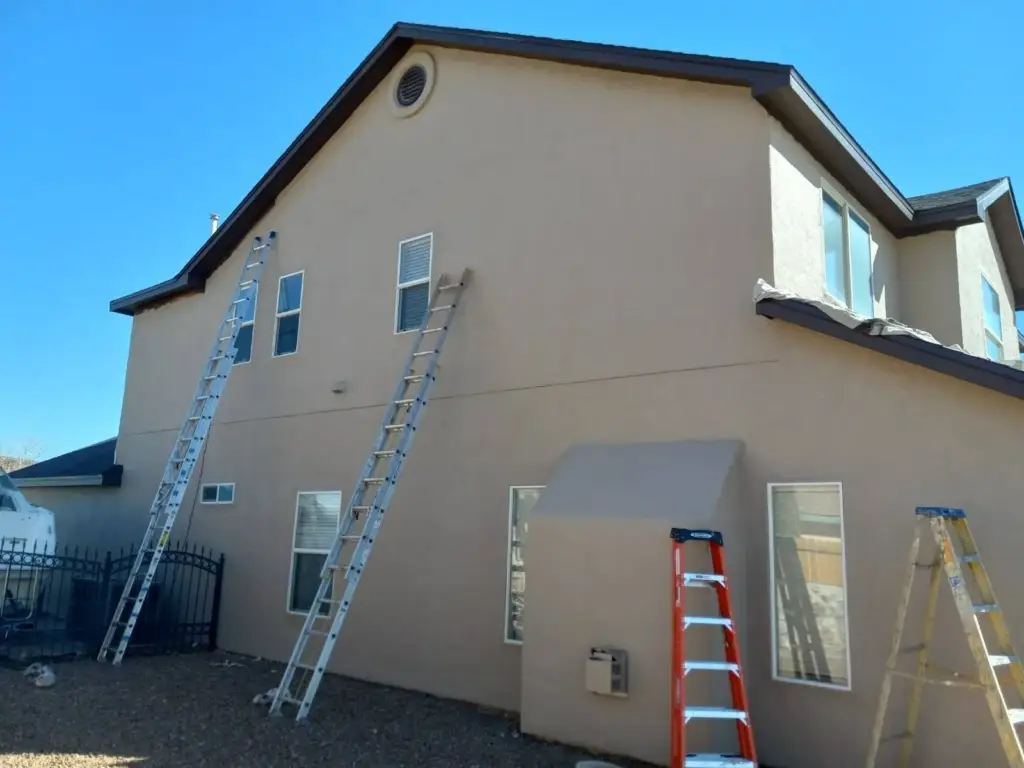 Two-story stucco house with ladders set against the wall for coating
