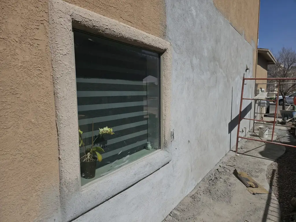 Stucco wall beside a window with a gray new base coat next to the old tan finish