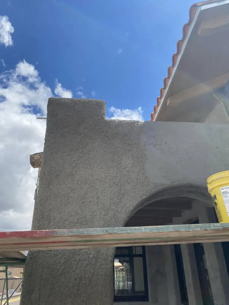 Close-up of a stepped parapet wall in fresh stucco brown coat against a blue sky