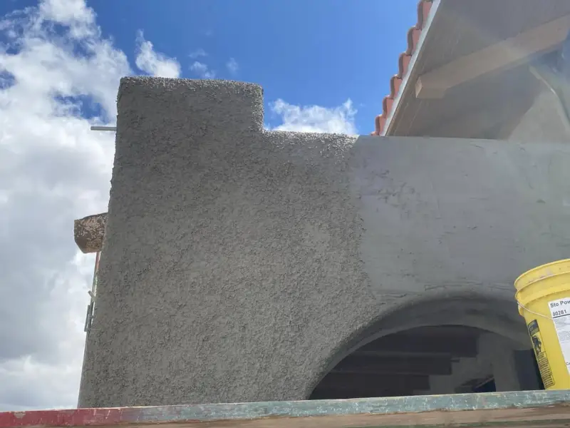 Close-up of a stepped parapet wall in fresh stucco brown coat against a blue sky