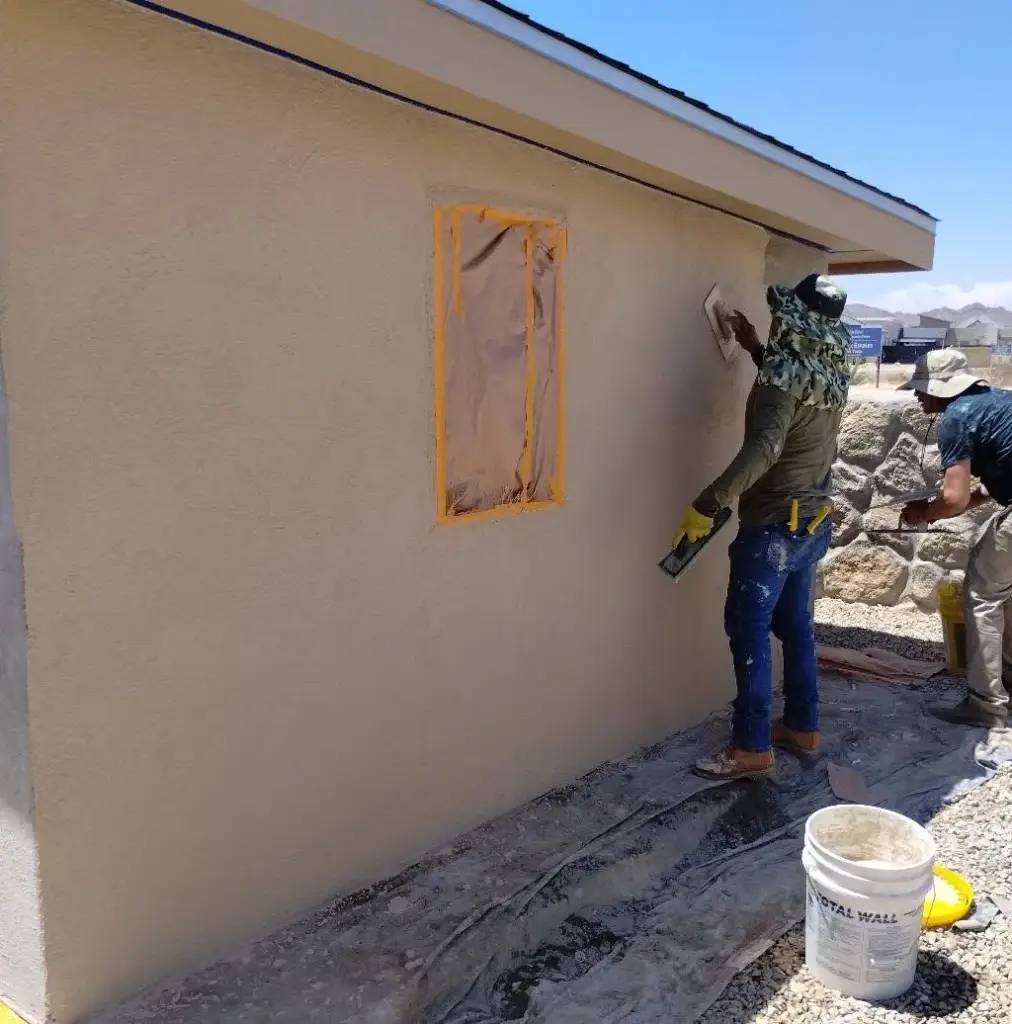 Worker texturing a masked stucco patch on a tan wall