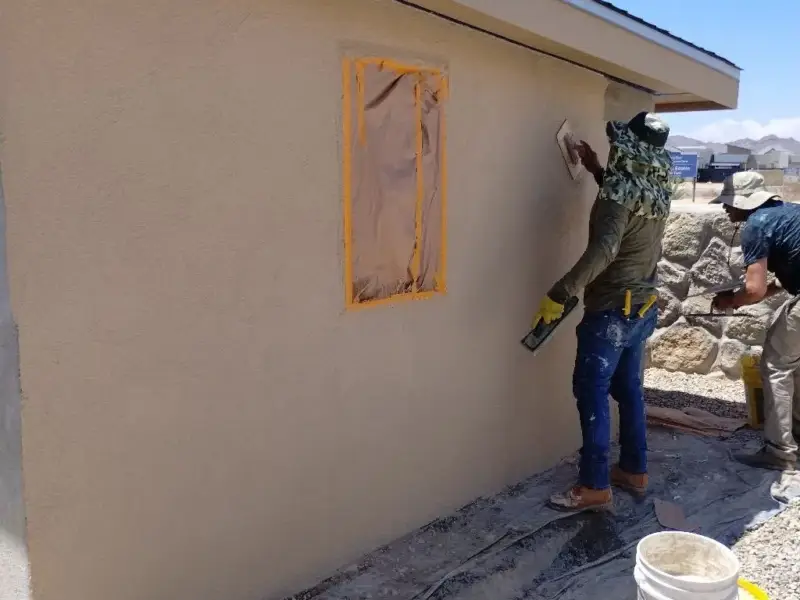 Worker texturing a masked stucco patch on a tan wall