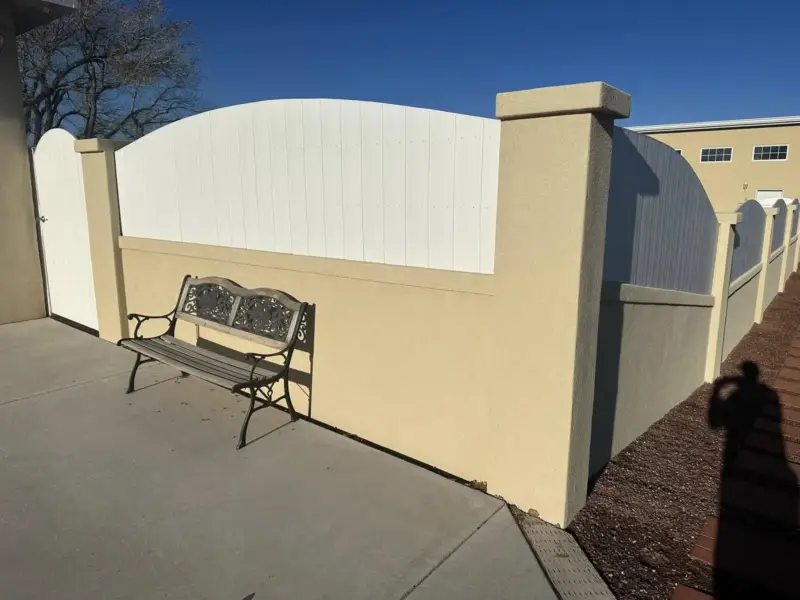 Finished tan stucco pillars and wall with a white fence and bench