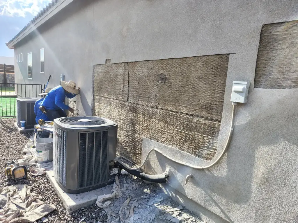 Section of stucco cut away behind an air conditioner showing the lath underneath